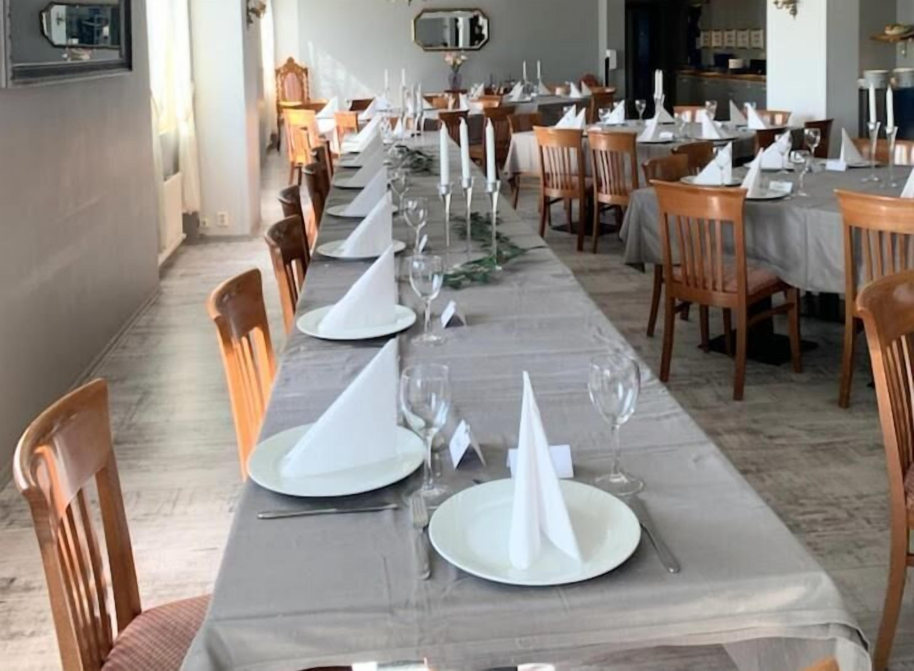 Uma longa mesa de jantar com toalhas brancas, cadeiras e pratos e copos organizados.