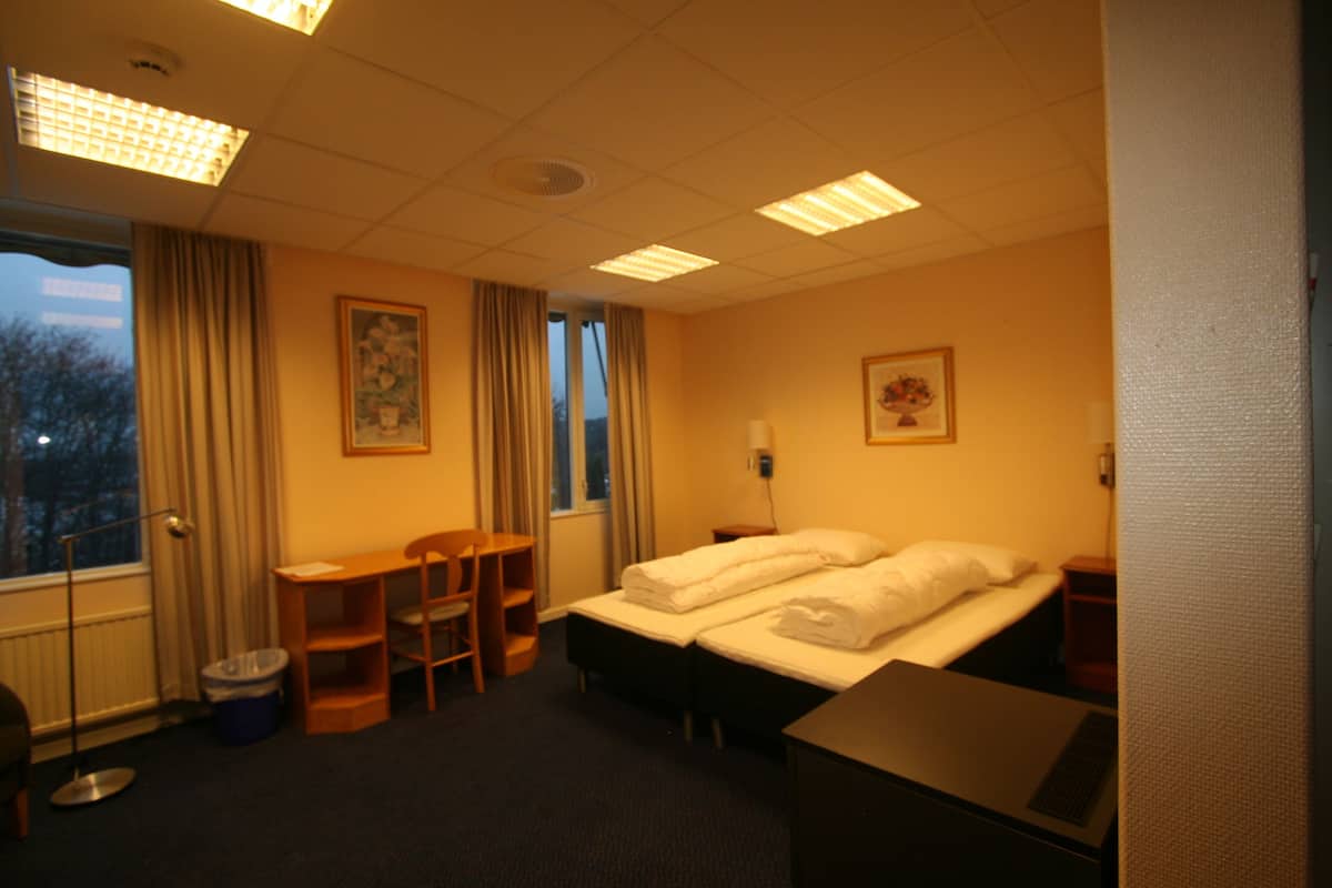 A hotel room with two beds, a desk, a chair, a window, and a picture on the wall.