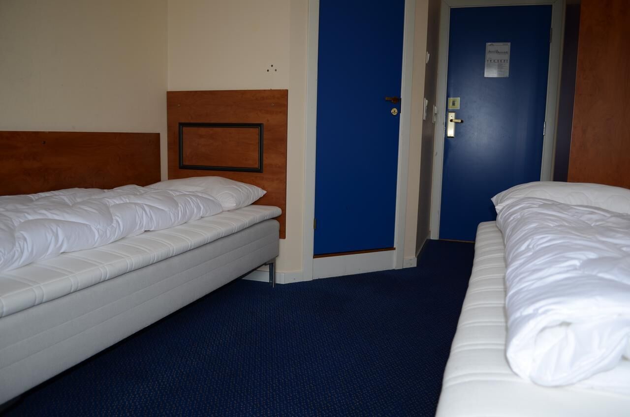 A hotel room with two single beds, a wooden headboard, a blue door, and a carpeted floor.