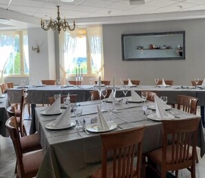 Un comedor con mesas dispuestas para el servicio, una araña y una estantería con objetos decorativos.