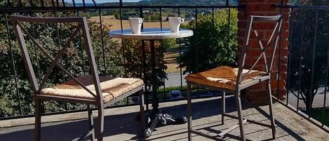 Un balcón con dos sillas y una pequeña mesa, con vistas a un paisaje pintoresco.