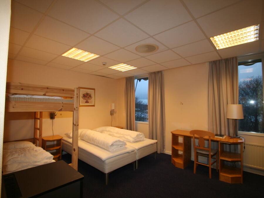 A hotel room with a bunk bed, a desk, a chair, a lamp, and a window with curtains.