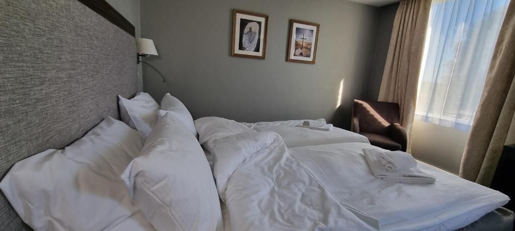 Una camera d'hotel con un letto, una sedia, una lampada e due quadri appesi al muro.