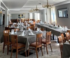Un amplio salón comedor con largas mesas dispuestas para varios invitados, sillas de madera y candelabros.