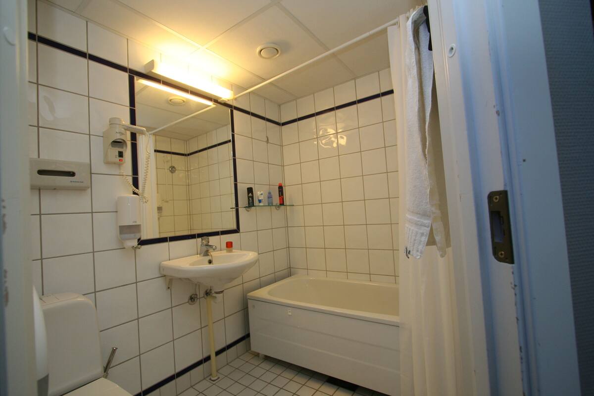 A bathroom with white tiles, a sink, a mirror, a toilet, and a bathtub.