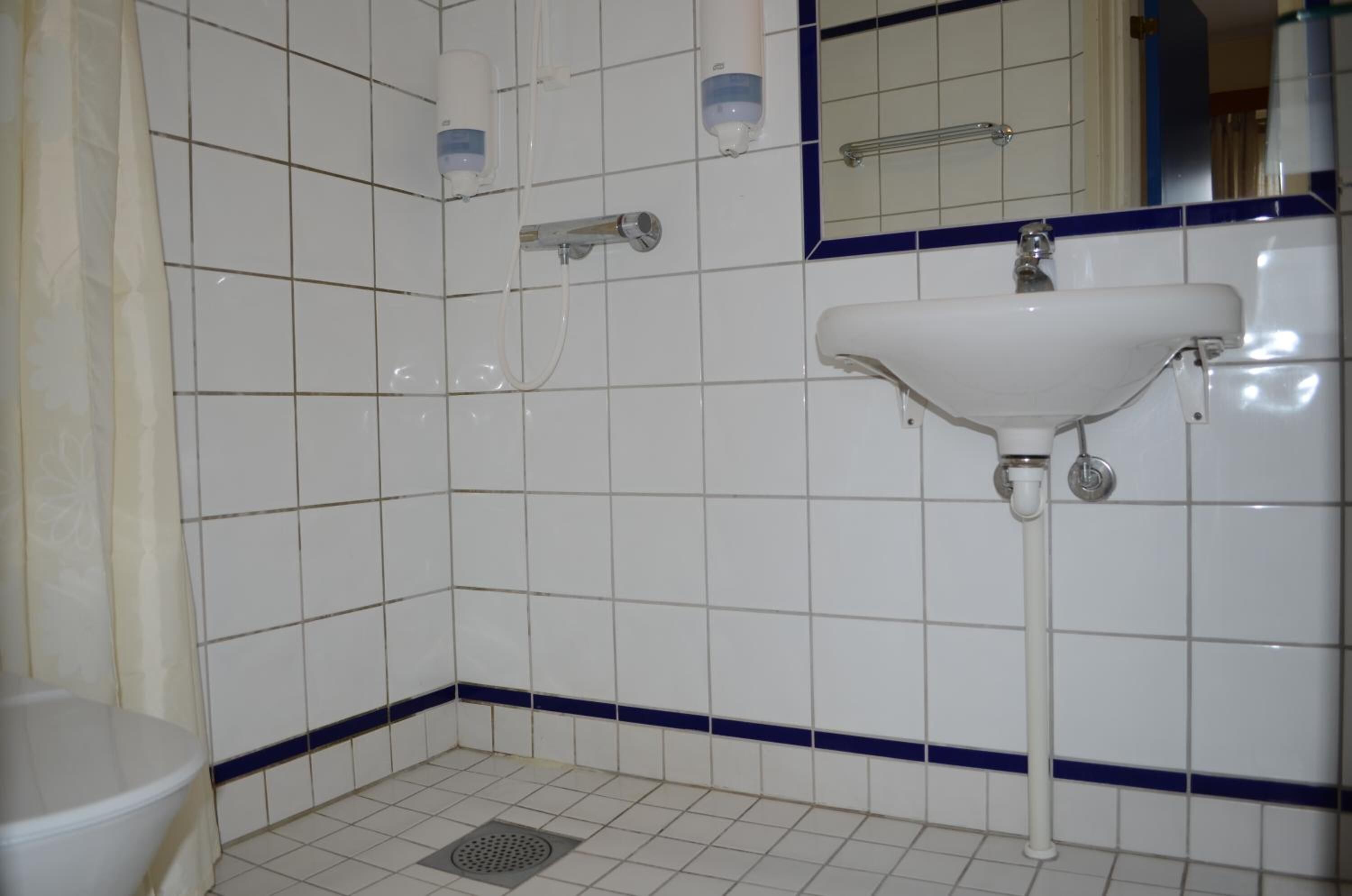 A bathroom with white tiles, a white sink, a mirror, and a showerhead.
