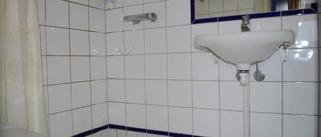 A bathroom with white tiles, a white sink, a mirror, and a showerhead.