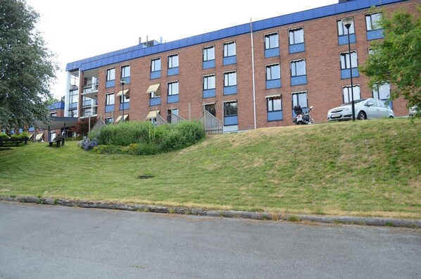 Un edificio de varios pisos con fachada de ladrillo y detalles azules, que cuenta con un área de estacionamiento con coches y un corredor cubierto.