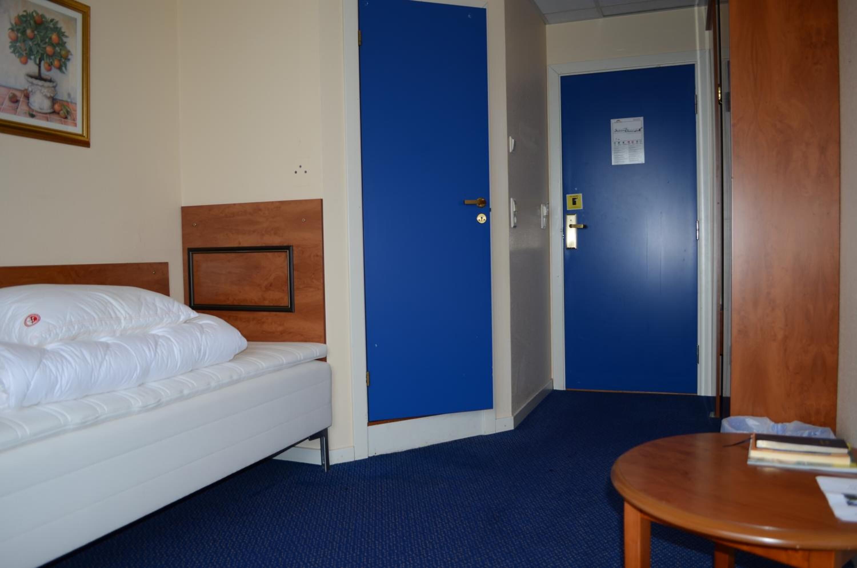 Una habitación de hotel con una cama, una mesita pequeña y una puerta azul.