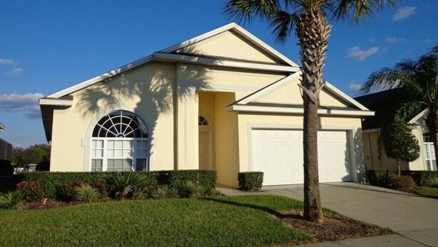 A single-story house with a garage, a large arched window, and a palm tree in the front yard. - Beautiful 4 Bed, 3.5 Bath Disney pool home. A Perfect family getaway! (Clermont)