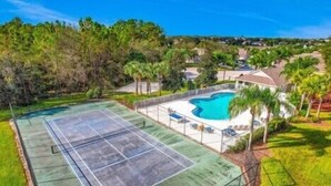 A tennis court with a pool, surrounded by palm trees and houses. - Beautiful 4 Bed, 3.5 Bath Disney pool home. A Perfect family getaway! (Clermont)