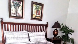 A neatly made bed with patterned bedding, two framed pictures on the wall, a bedside lamp, and a potted plant. - Beautiful 4 Bed, 3.5 Bath Disney pool home. A Perfect family getaway! (Clermont)