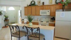 A kitchen with wooden cabinets, a white refrigerator, a microwave, and a dining area with two chairs. - Beautiful 4 Bed, 3.5 Bath Disney pool home. A Perfect family getaway! (Clermont)