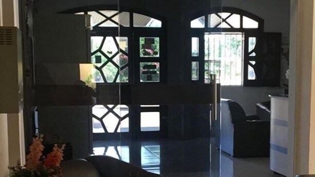 A modern living room with a black leather sofa, a small table with a vase of flowers, and a glass partition with geometric patterns. - Hotel Brasilia (Buriticupu)