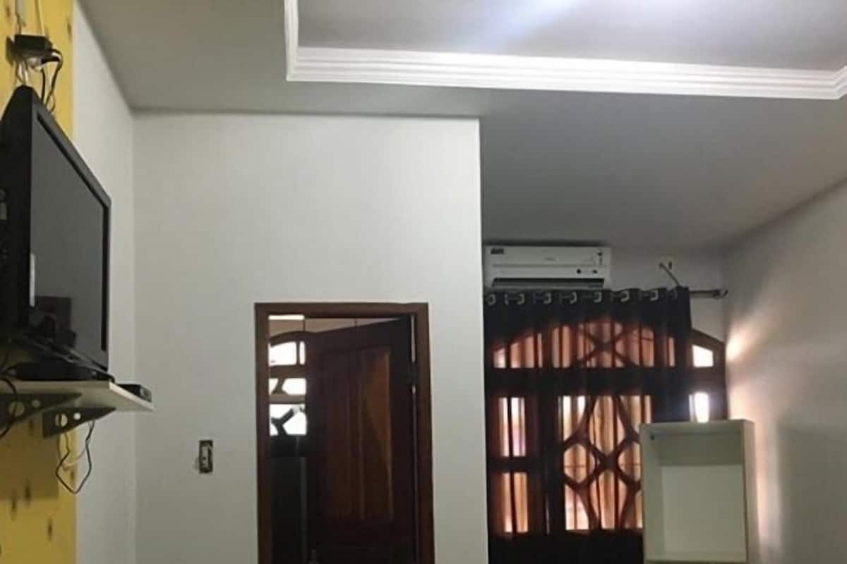 Een kleine, eenvoudig ingerichte kamer met een bed, bureau, stoel, televisie en een airconditioning.