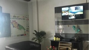 A living room with a black leather sofa, a glass coffee table, a TV mounted on the wall, a small plant, and a map on the wall. - Hotel Brasilia (Buriticupu)