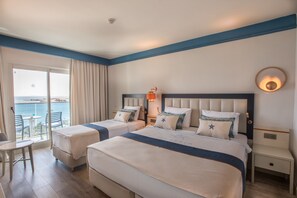 Une chambre d’hôtel avec deux lits, un balcon avec une table et des chaises, et une vue sur la mer.
