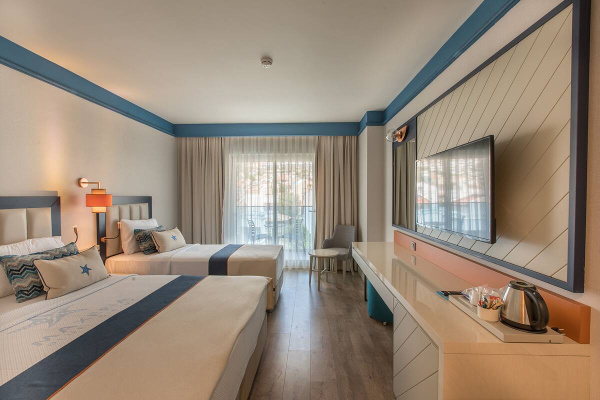A hotel room with two beds, a TV, a small table, and a window with curtains.