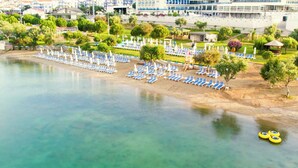 Vue aérienne d’un complexe hôtelier en bord de mer, avec des rangées de chaises longues et de parasols, une petite piscine et un kiosque.