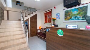 Un área de recepción con un escritorio de madera, un mostrador de entrada y salida, una escalera y un cuadro en la pared.