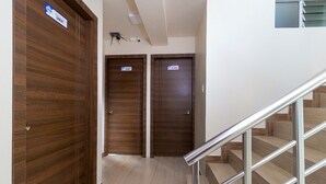 Un pasillo de hotel con dos puertas de madera, cada una con un cartel que indica el tipo de habitación. Se ve una escalera de metal con barandilla a la derecha.