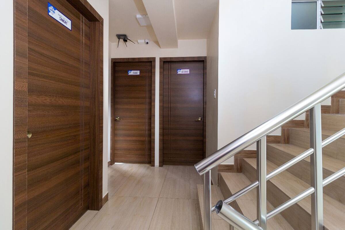 A hotel hallway with two wooden doors, each marked with a sign indicating a room type. A metal staircase with a handrail is visible to the right.
