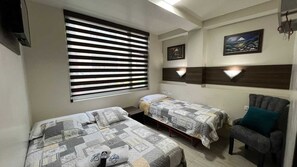 A room with two single beds, a chair, a window with blinds, and a wall-mounted picture. - Hotel La Cumbre by Team Adventure (Baños de Agua Santa)