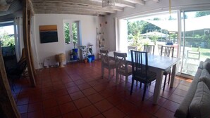 Un ampio soggiorno con pavimento piastrellato, un tavolo da pranzo e sedie. Una grande finestra offre vista sull'esterno.