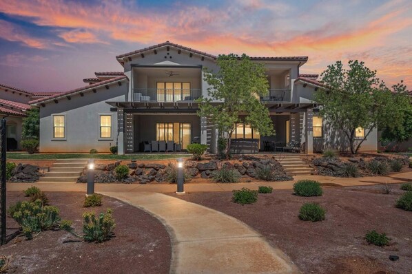 A two-story house with a covered patio, a landscaped garden, and a clear sky.