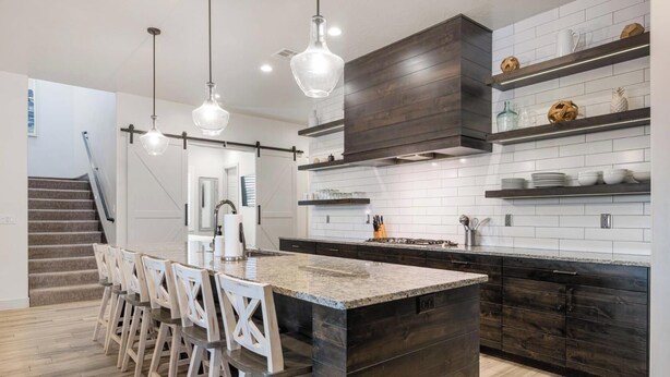 Une cuisine moderne dotée d’un îlot central, de tabourets de bar, de luminaires suspendus et d’un escalier menant à un autre niveau.