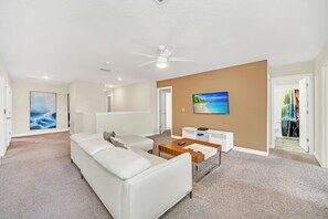 A spacious living room with a white sofa, a coffee table, and a TV mounted on the wall.