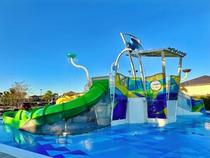 A water park with a green slide, a water fountain, and a pool with blue tiles.