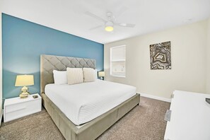 Un dormitorio con cama, mesita de noche, lámpara, ventilador de techo y una obra de arte en la pared.