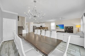 Una cocina moderna con armarios blancos, una isla central y un comedor con una gran mesa de madera y sillas blancas.