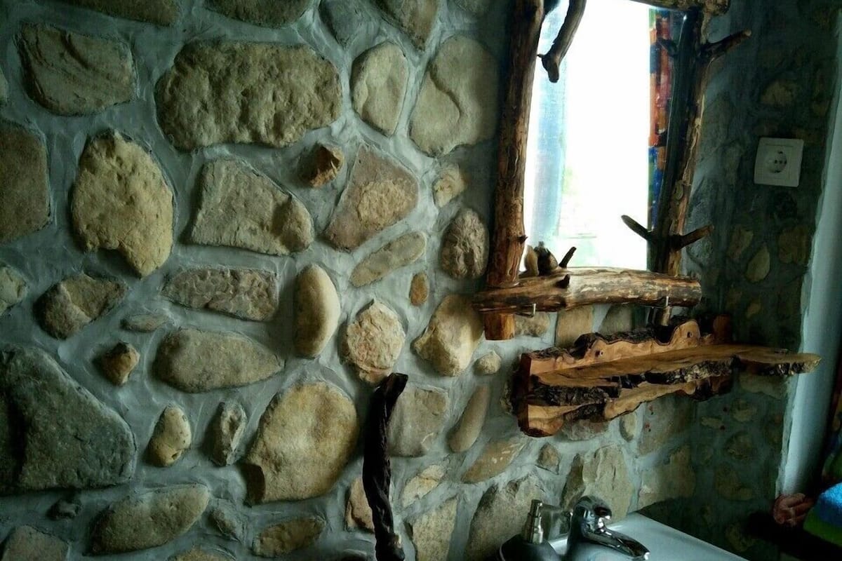 A stone wall with a rustic wooden shelf and a white sink.
