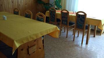 Un comedor con una mesa cubierta con mantel amarillo, sillas de madera con cojines estampados y una planta grande al fondo.