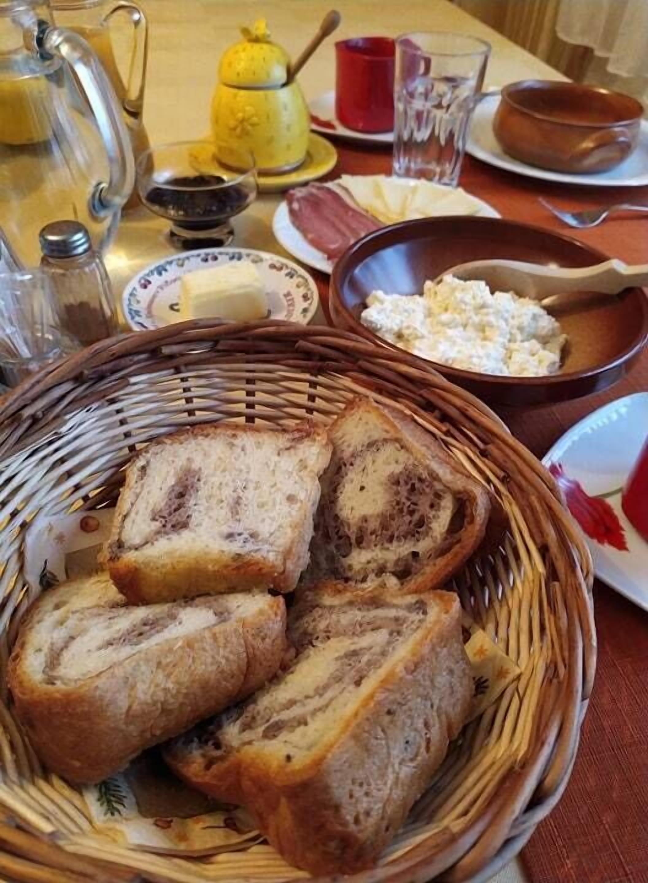 A table with a basket of sliced bread, a bowl of cottage cheese, and a teapot.