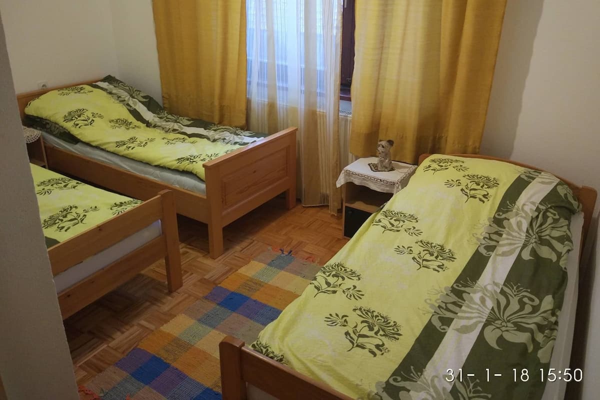 A small, cozy room with two wooden beds, a small table with a figurine, and a colorful checkered rug.