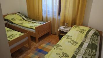 A small, cozy room with two wooden beds, a small table with a figurine, and a colorful checkered rug.