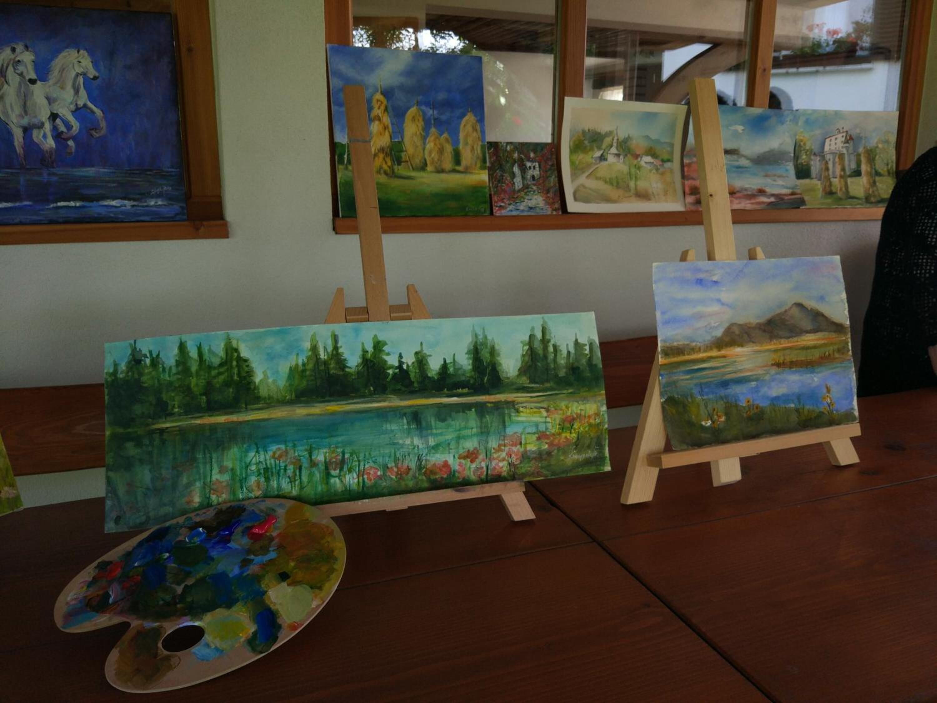A wooden table with several paintings and a palette.