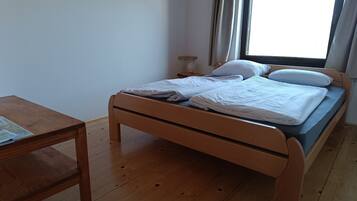 A single bed with a wooden frame and a blue mattress, a wooden nightstand with a lamp, and a small table with a map.