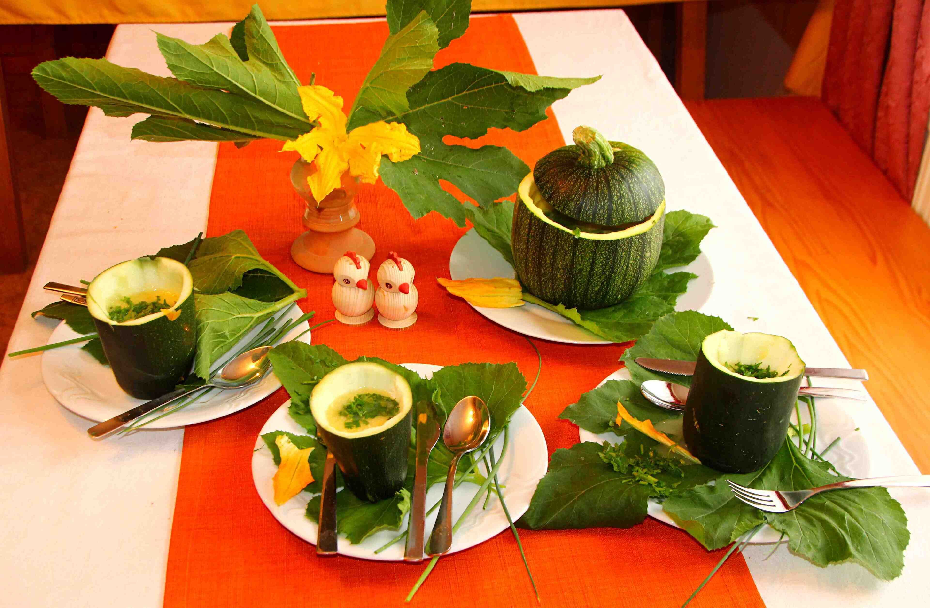 Ein Tisch mit vier kürbisschenförmigen Schalen, gefüllt mit grüner Soße, und Blättern sowie Besteck.