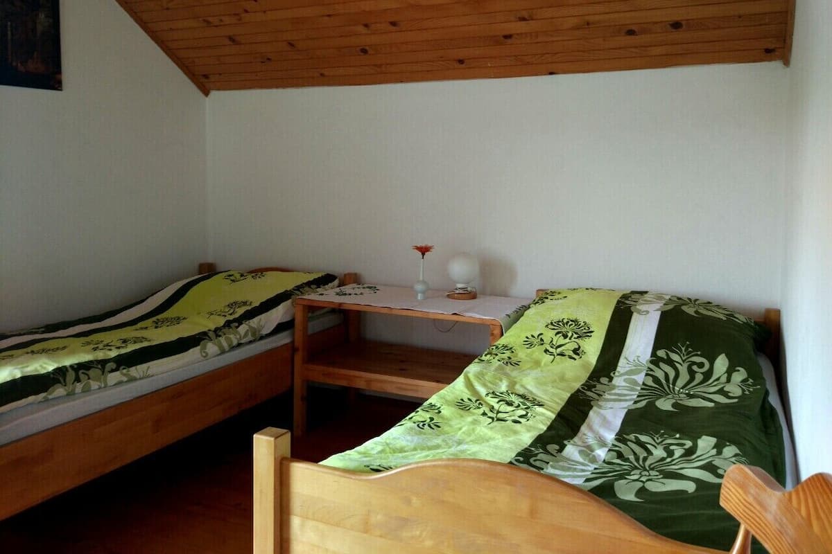 A small, cozy room with two wooden bunk beds, a small table with a vase and a lamp, and a wooden ceiling.