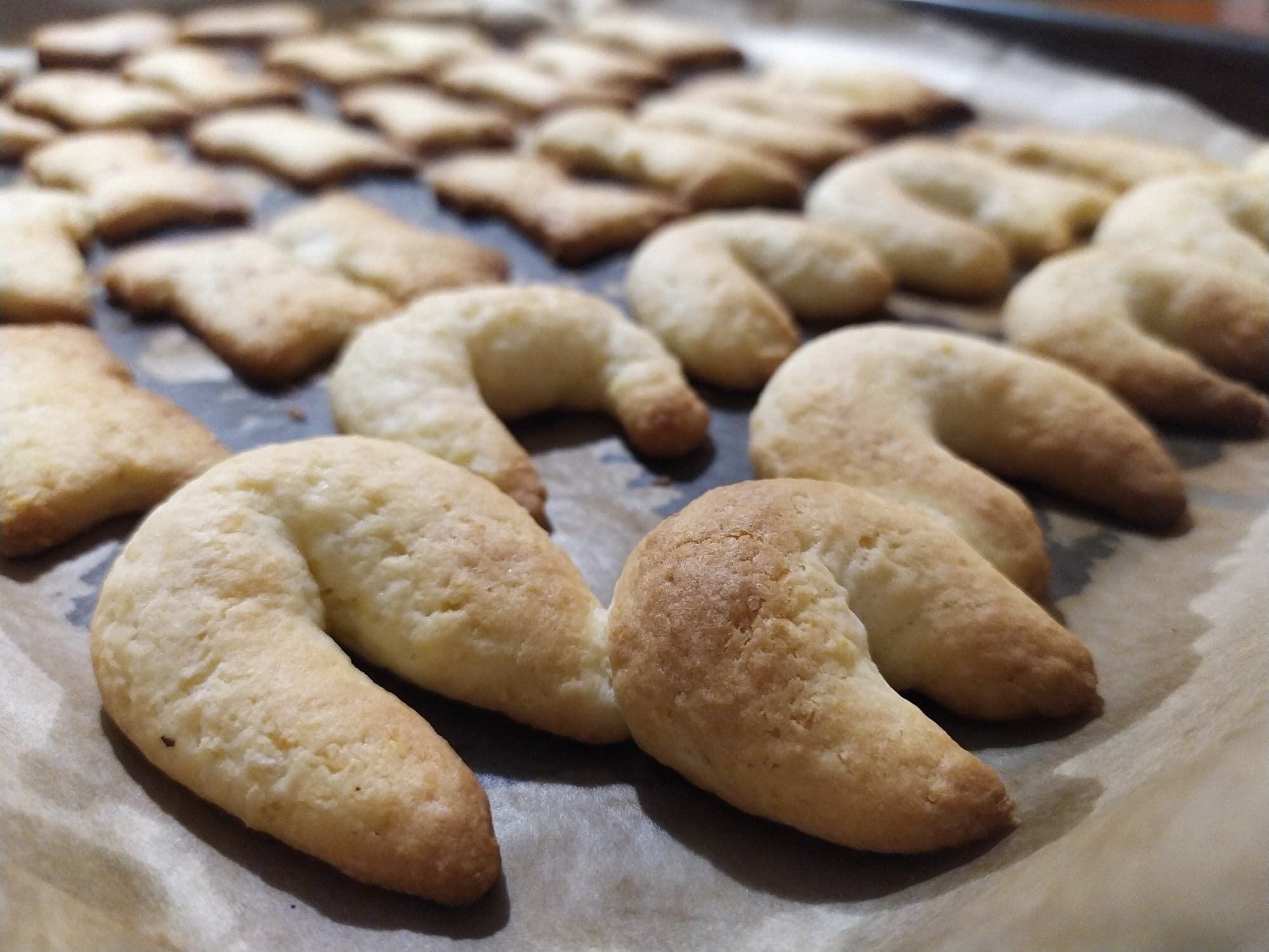 A tray of baked goods, including crescent-shaped pastries and rectangular cookies, on parchment paper.