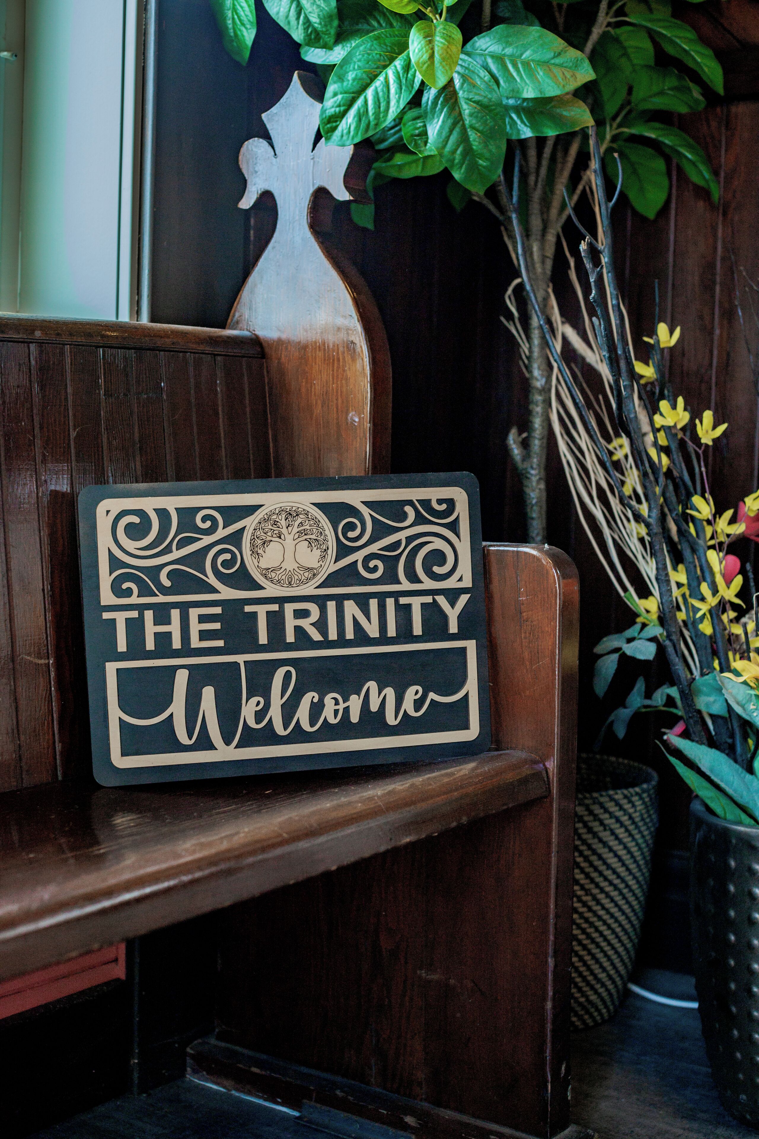 Eine hölzerne Bank mit einem Schild, auf dem 'The Trinity Welcome' steht.