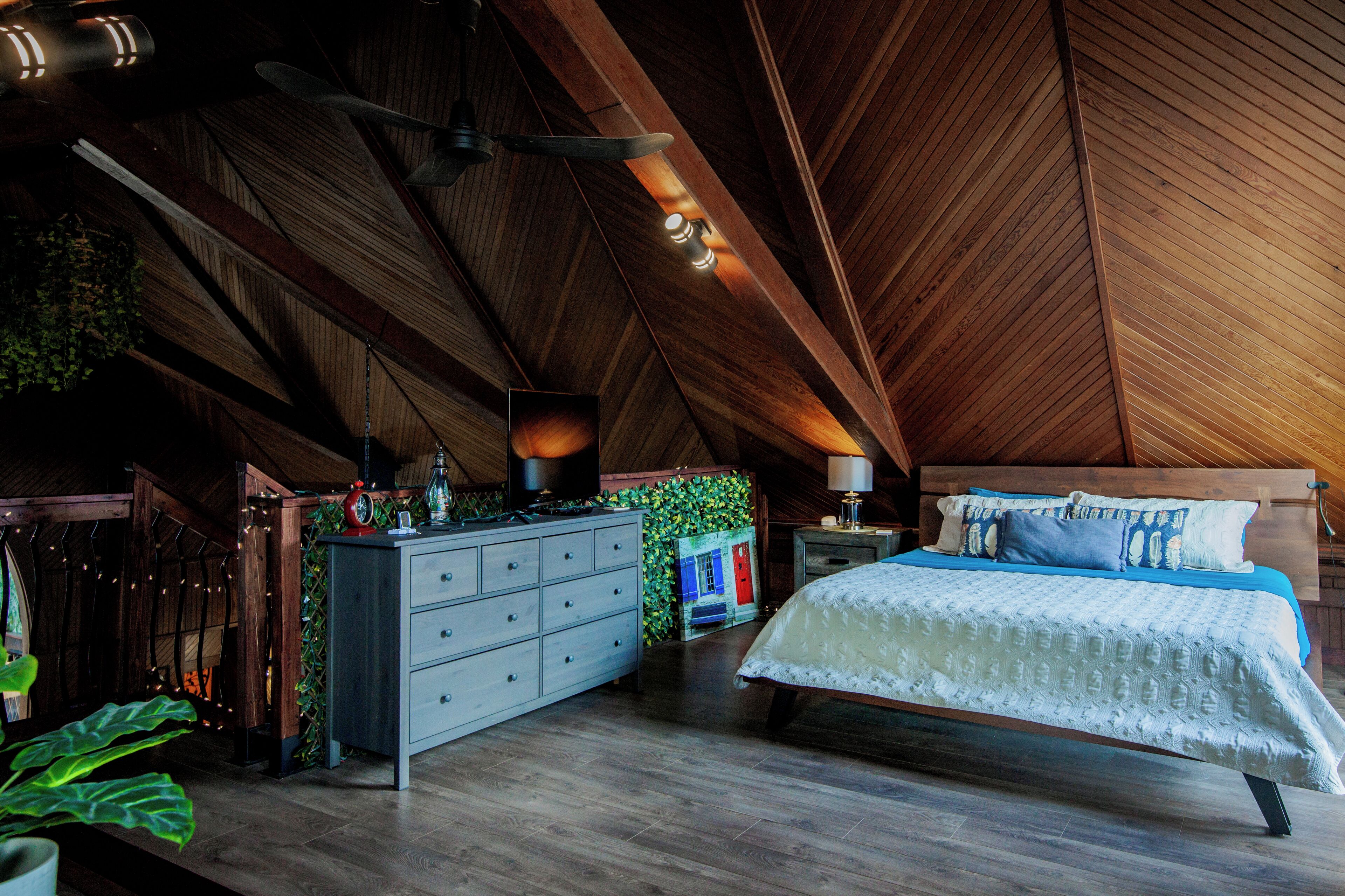 A bedroom with a wooden ceiling, a bed with white bedding, a dresser, and a nightstand.