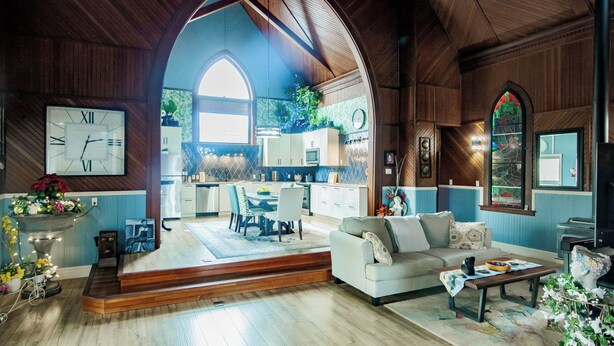 A spacious living room with a large arched doorway leading to a kitchen, wooden flooring, and a cozy seating area with a sofa and coffee table.
