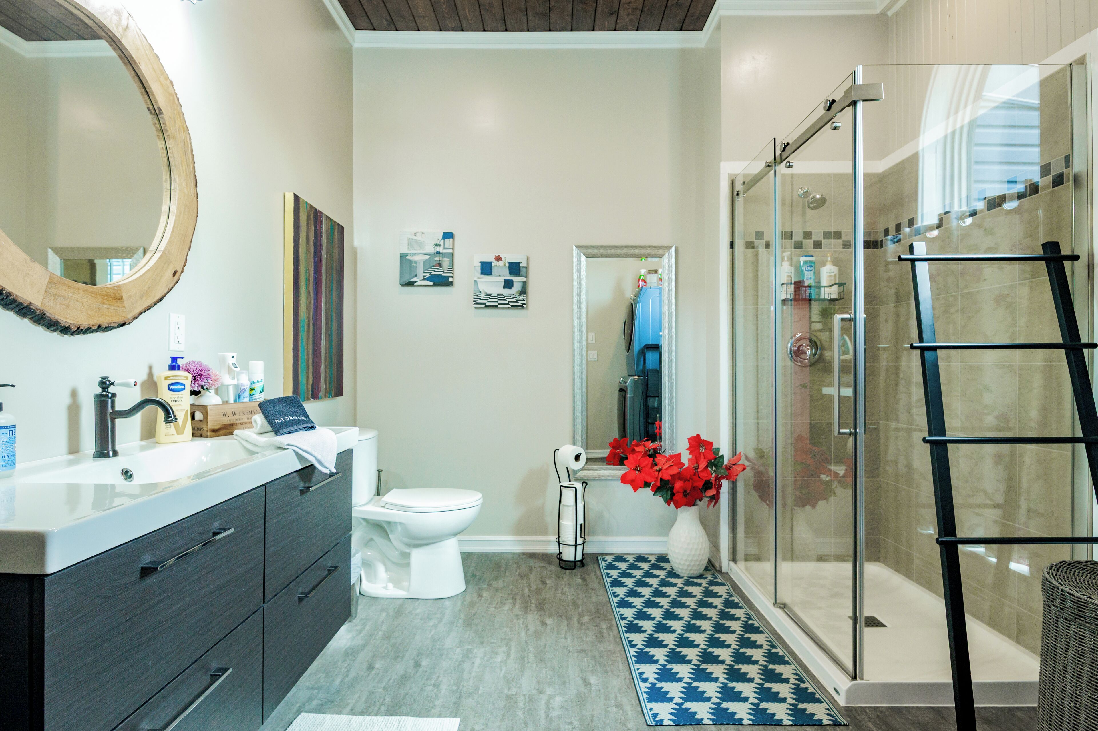 Un baño moderno con un espejo grande, un inodoro blanco, una ducha con puerta de vidrio y una escalera negra.