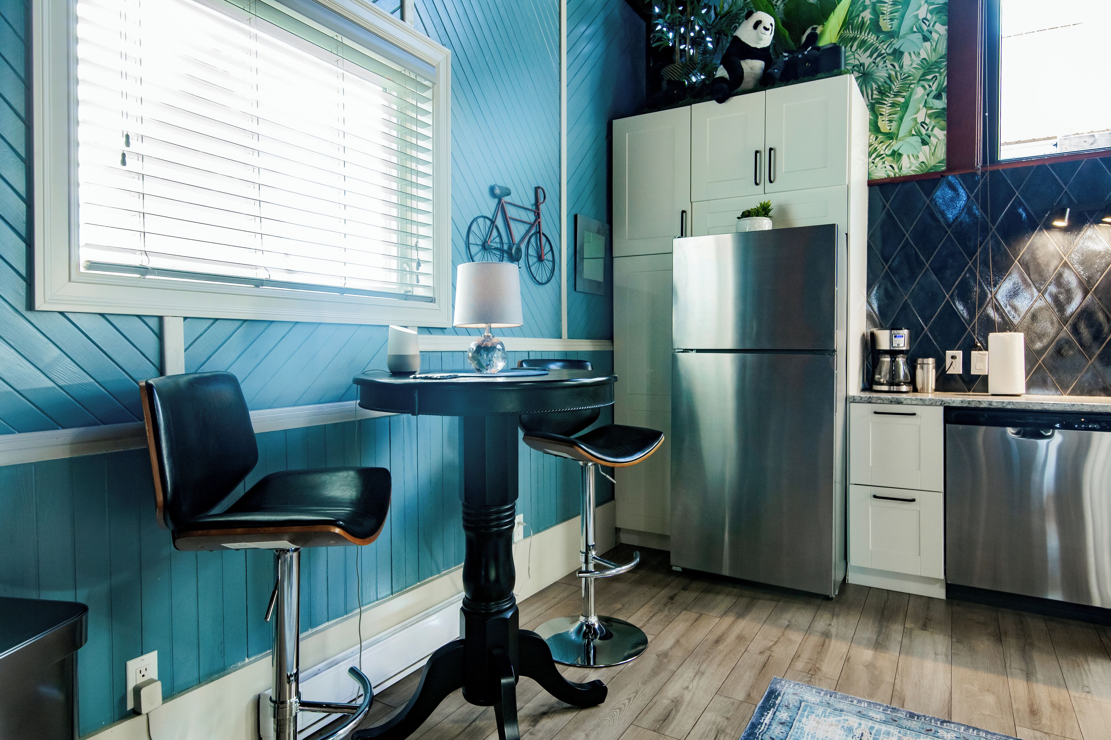 Una cocina con pared azul, un refrigerador, una estufa y una ventana con persianas.