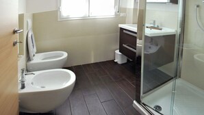 Un baño moderno con inodoro, bidé, lavamanos y ducha con mampara de vidrio.